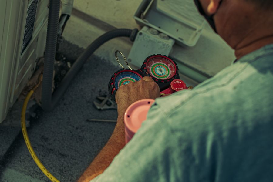Technician servicing an AC condenser with refrigerant gauges