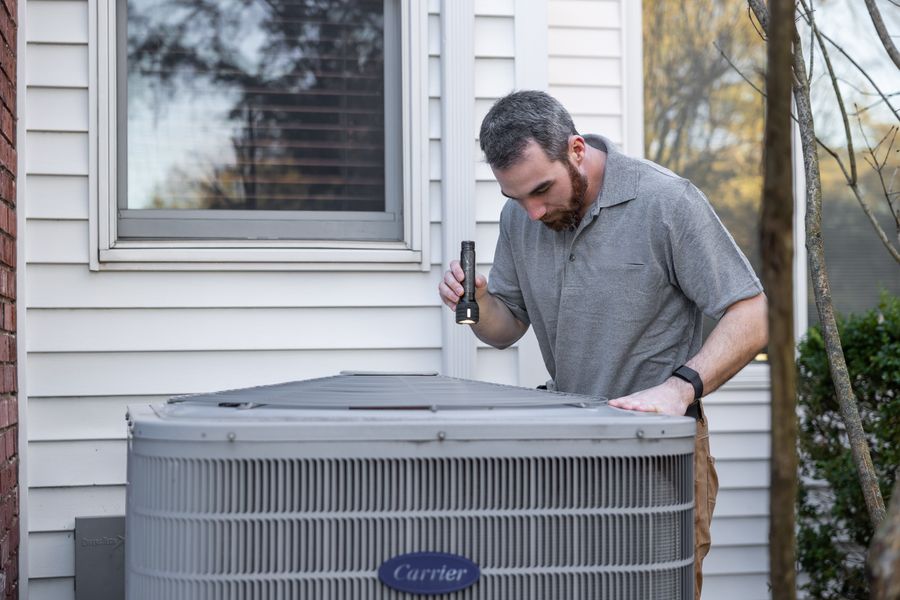 Technician inspecting a residential AC condenser unit beside a home